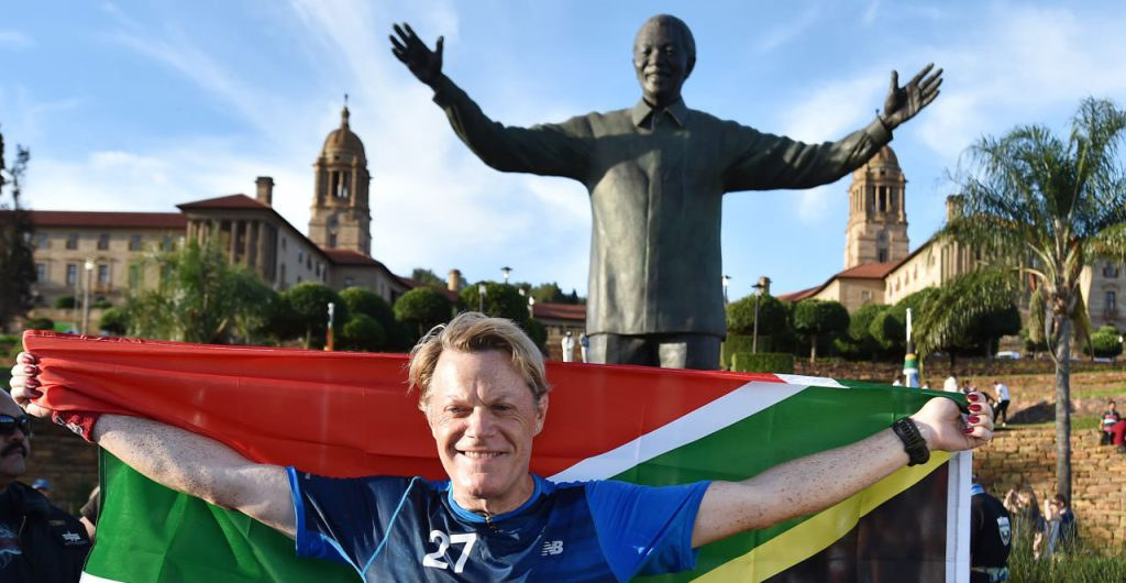 British comedian Eddie Izzard holds a South African flag beneath a statue of former president Nelson Mandela at the government’s Union Buildings in Pretoria, South Africa, Sunday, March 20, 2016. (AP Photo)